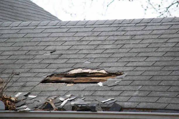 Roof of a residential house showing damage, multiple layers of shingles, missing shingles