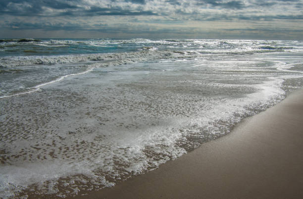 Changing Tide Incoming waves cover the beach as a dark sky begins to lighten at Cape Hatteras National Seashore. ebb and flow stock pictures, royalty-free photos & images