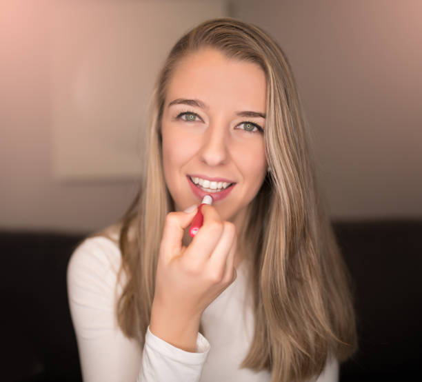 istock pretty blonde young woman applying her lip gloss, make up 937568760