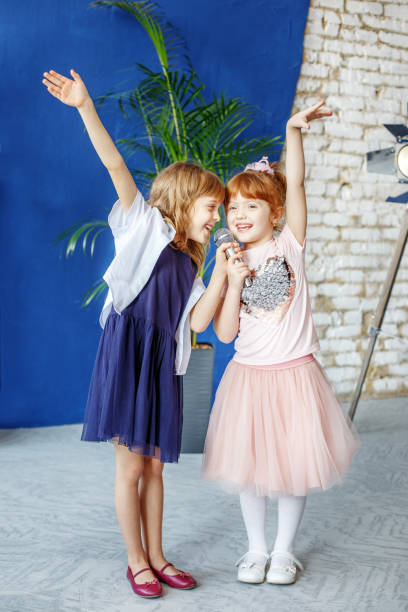 two little smiling kids dance and sing a song in karaoke. the co - circular skirt fotos imagens e fotografias de stock