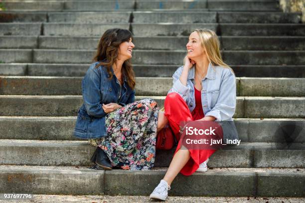 Two Young Women Talking And Laughing On Urban Steps Stock Photo - Download Image Now