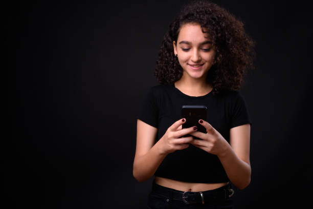 using phone Portrait Of Beautiful Teenager Girl Against Black Background iranian ethnicity stock pictures, royalty-free photos & images