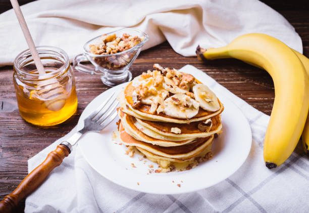 Pancakes with banana, walnuts and honey Pancakes with banana, walnuts and honey. Healthy breakfast. On dark wooden table background. pancake photos stock pictures, royalty-free photos & images