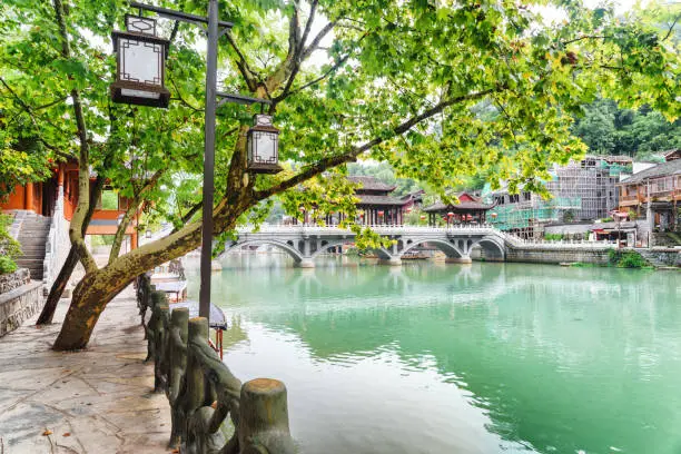 Wonderful view of the Tuojiang River among green trees in Phoenix Ancient Town (Fenghuang County), China. Scenic bridge is visible in background. Fenghuang is a popular tourist destination of Asia.