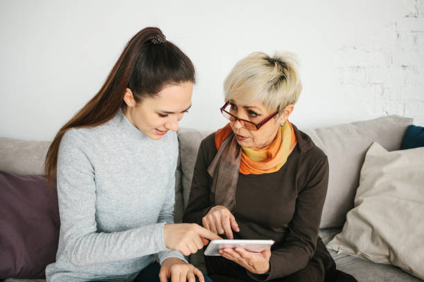 una joven a una anciana, explica cómo usar una tableta o muestra alguna aplicación te enseña cómo usar una red social. enseñando a la generación más vieja de las nuevas tecnologías. - grandmother granddaughter senior adult teenager fotografías e imágenes de stock