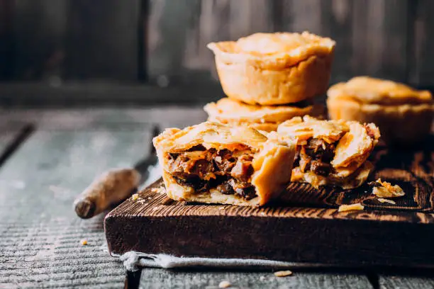 Photo of Fresh Traditional Australian meat mini pie on the wooden board on table background, closeup with copy space, rustic style