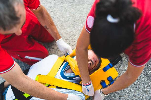 Paramedic, emergency, ambulance staff and medical help. Ambulance staff member assisting injured person with transport stretcher. Paramedics assisting injured person first aid on road