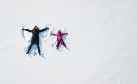 Muchacha del niño y la madre jugando y hacer un ángel de nieve en la nieve. Vista superior del plano arriba photo