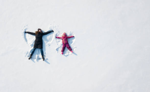 muchacha del niño y la madre jugando y hacer un ángel de nieve en la nieve. vista superior del plano arriba - recreational pursuit leisure activity relaxation fun fotografías e imágenes de stock