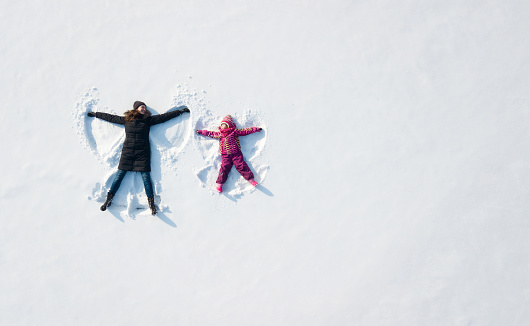 Child girl and mother playing and making a snow angel in the snow. Top flat overhead view