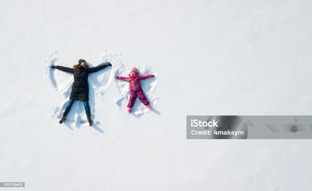 Child girl and mother playing and making a snow angel in the snow. Top flat overhead view Winter Stock Photo