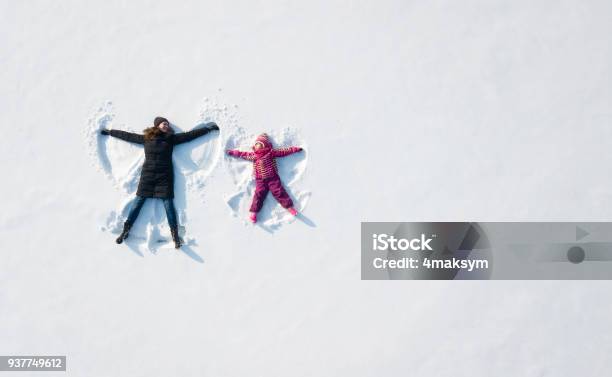 Child Girl And Mother Playing And Making A Snow Angel In The Snow Top Flat Overhead View Stock Photo - Download Image Now