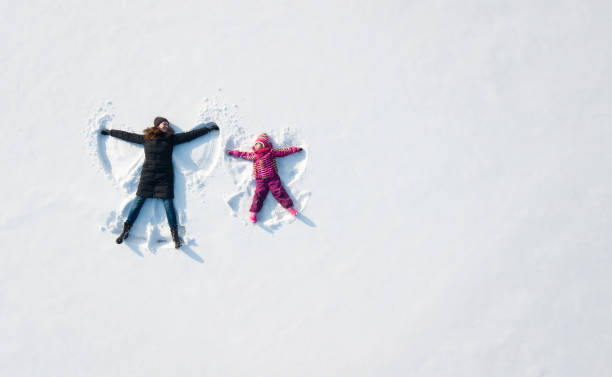 garota de criança e mãe jogando e fazendo um anjo de neve na neve. vista aérea plana superior - winter family child snow - fotografias e filmes do acervo