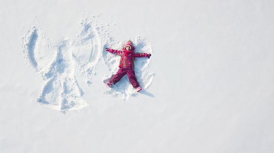 Child girl playing and making a snow angel in the snow. Top flat overhead view