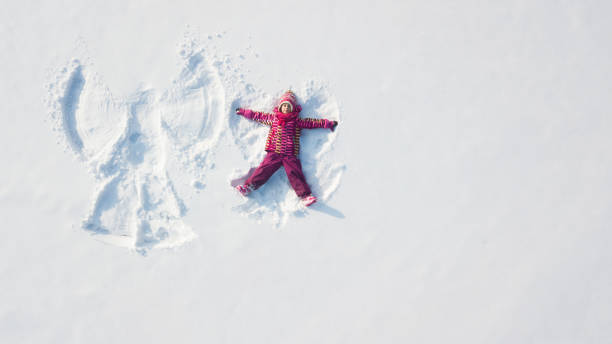 Child girl playing and making a snow angel in the snow. Top flat overhead view Child girl playing and making a snow angel in the snow. Top flat overhead view snow angels stock pictures, royalty-free photos & images
