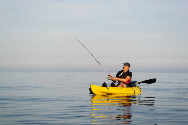 Fishing on calm and sunny seas A man on a sea kayak fishes and enjoys the warmth of summer on mirror flat sea rowing boat fishing stock pictures, royalty-free photos & images