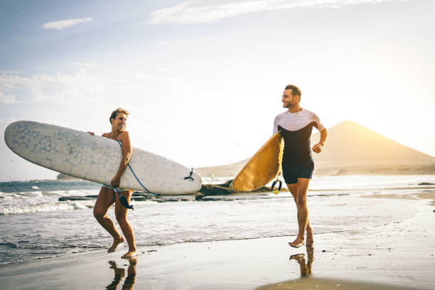 jeune couple de surfeurs en cours d’exécution avec des planches de surf sur la plage au coucher du soleil - heureux amants passe au filtre de vintage - notion de peuple, de sport et de mode de vie - ensemble surf - mettre l’accent sur le conseil de femme - surfing men hawaii islands wave photos et images de collection