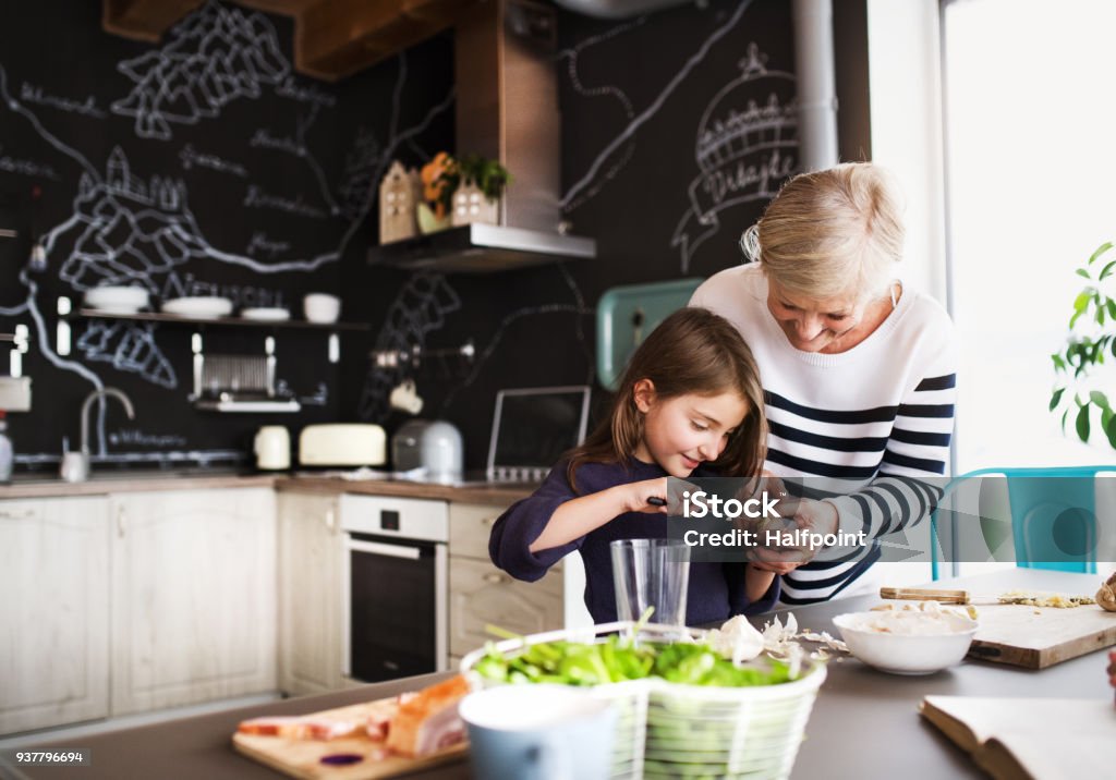 A small girl with grandmother cooking at home. A small girl with her grandmother at home, cooking. Family and generations concept. Grandmother Stock Photo