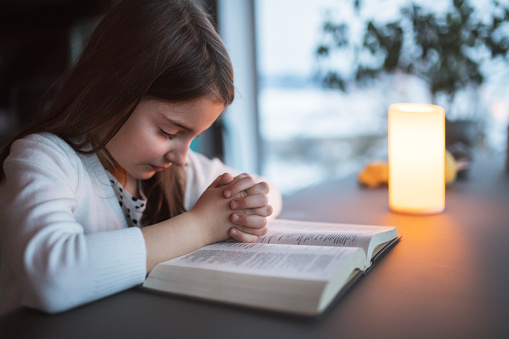 A small girl with bible at home, praying.