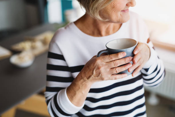 年配の女性が台所でコーヒー カップを保持しています。 - tea women cup drinking ストックフォトと画像