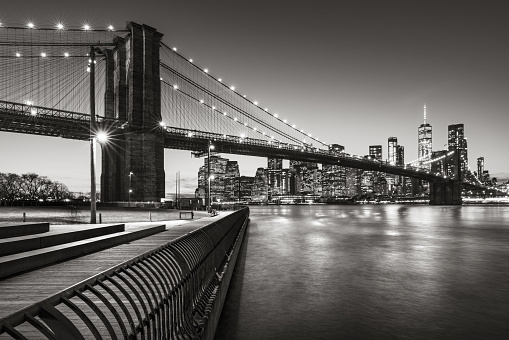 Brooklyn Bridge Park boardwalk in evening with the skyscrapers of Lower Manhattan, East River, and the Brooklyn Bridge in Black & White. Brooklyn, New York City