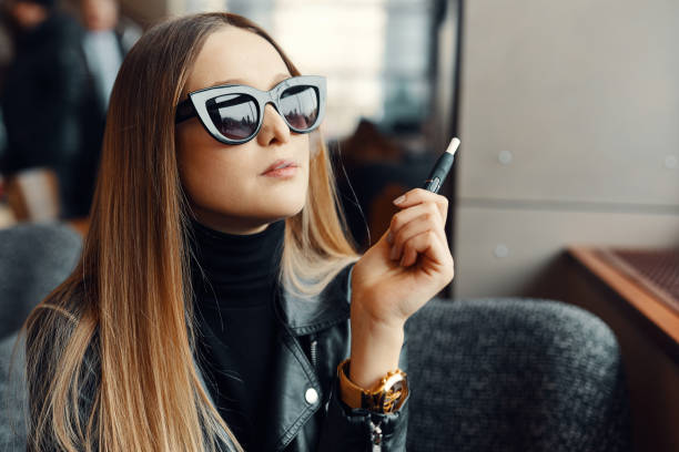 dziewczyna siedzieć w caffee miejsce i dymu elektronicznego papierosa nosić okulary - caffee zdjęcia i obrazy z banku zdjęć