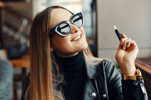 dziewczyna siedzieć w caffee miejsce i dymu elektronicznego papierosa nosić okulary - caffee zdjęcia i obrazy z banku zdjęć