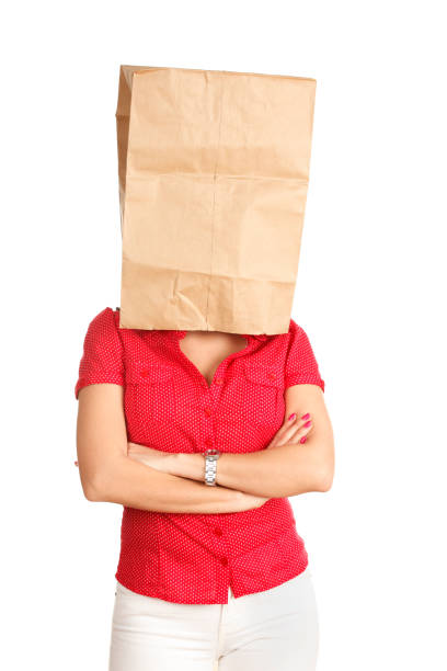 A young woman with a grocery bag over her head and arms crossed.
