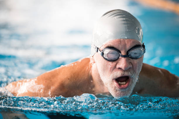 senior homme nager dans une piscine couverte. - active seniors retirement enjoyment swimming pool photos et images de collection