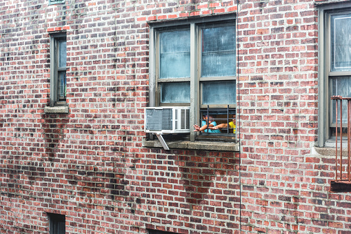 Bronx, USA - October 29, 2017: Brick apartment condo building architecture in Fordham Heights, Bronx, NYC, Manhattan, New York City, fire escapes, windows, ac units during rain, kids children playing, reaching arms through window