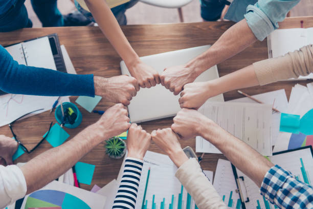 Close up cropped photo of partners putting their fists together in a circle on top of the table with work stuff. Trust, friendship, unity, cooperation concept Close up cropped photo of partners putting their fists together in a circle on top of the table with work stuff. Trust, friendship, unity, cooperation concept recruitment team stock pictures, royalty-free photos & images