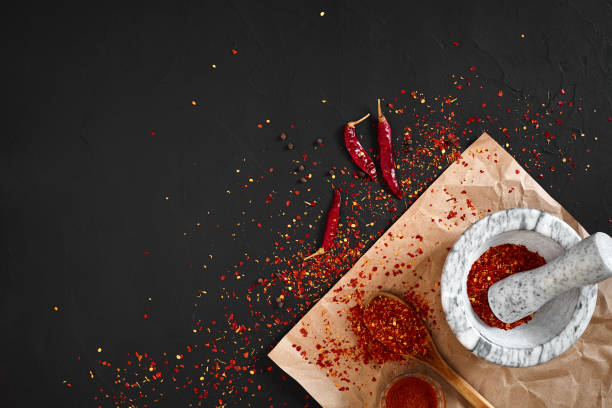 Dried and crushed red chili pepper in stone mortar on black background. Copy space. Top view. Still life. Flay lay