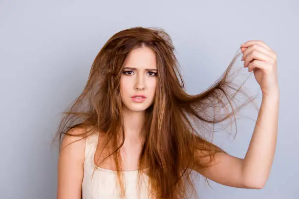 Photo of Close up portrait of frustrated young girl with messed hair on pure  background, wearing white casual singlet, holding her hair