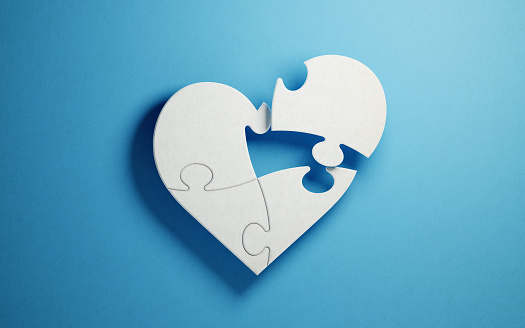White jigsaw puzzle pieces are forming a heart shape on blue background. Horizontal composition with copy space. Clipping path is included.