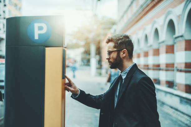 Businessman using Parking Meter outdoors Bearded serious man entrepreneur in eyeglasses and a formal suit is using parking pay station terminal; handsome businessman in glasses and with the beard paying his parking time via automatic kiosk parking meter stock pictures, royalty-free photos & images