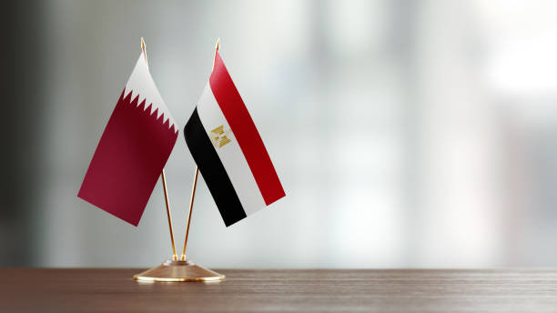 Qatari and Egyptian Flag Pair On A Desk Over Defocused Background