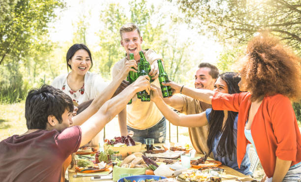 young multiracial friends toasting at barbecue garden party - friendship concept with happy people having fun at backyard bbq summer camp - food and drinks fancy picnic lunch - focus on beer bottles - picnic family barbecue social gathering imagens e fotografias de stock
