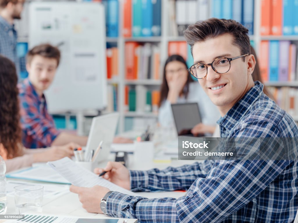 Startups, students and new business Young confident businessman posing in the office and start up team working together in the background, innovation and entrepreneurship concept Adult Stock Photo