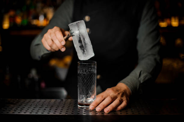 istock Bartender putting a big ice cube into an empty glass on a bar counter 937902258
