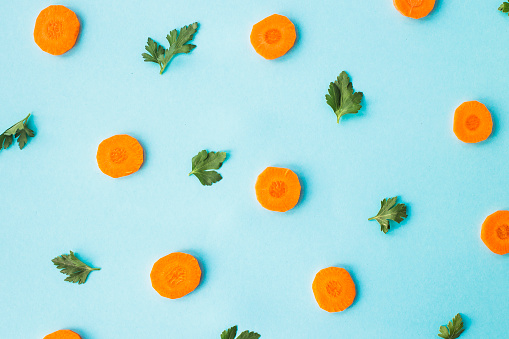 Bright round ringlets of carrots with green parsley sprigs on a blue background. Top view, flat lay