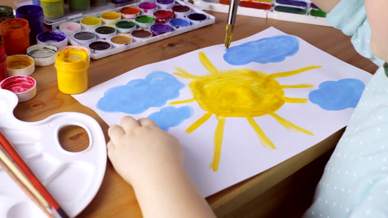 Young girl drawing yellow sun and blue clouds