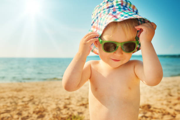 istock little boy smiling at the beach in hat with sunglasses 937914528