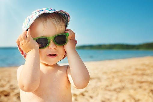 little boy smiling at the beach in hat with sunglasses