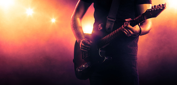 Male hands holding a guitar. Spotlight