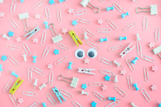 istock Cheerful pattern. Stationery chaotically scattered on a pale pink background. Doll eyes in the center of the confusion of clips, asterisks, clothespins and buttons. 937929504