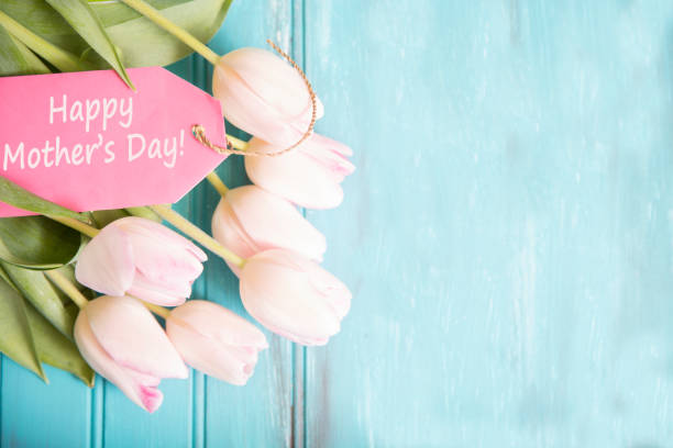 Happy Mother's Day flower bouquet in pink. Happy Mother's Day pink tulip flower bouquet on blue wooden background.   "Happy Mother's Day" message on pink note tag. gift tag note photos stock pictures, royalty-free photos & images