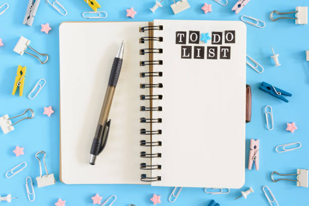 istock Photo from the top with scattered stationery. Open notebook on springs with white sheets. Inscription To Do List. Clips, clerical buttons and asterisks in a mess on a blue background. 937929812