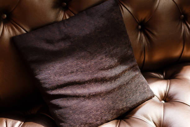 Vintage luxurious brown leather sofa with three fabric pillows.