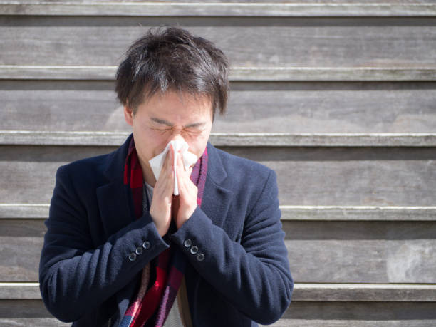 Asian Businessman Blowing His Nose Outdoors Young Japanese businessman has hay fever. He needs to blow his nose often. facial tissue photos stock pictures, royalty-free photos & images