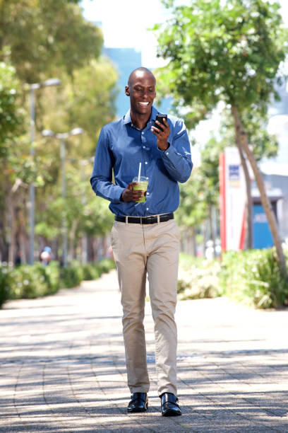 полное тело счастливый афро-американец ходить с мобильного телефона снаружи - smart casual occupation casual healthy eating стоковые фото и изображения